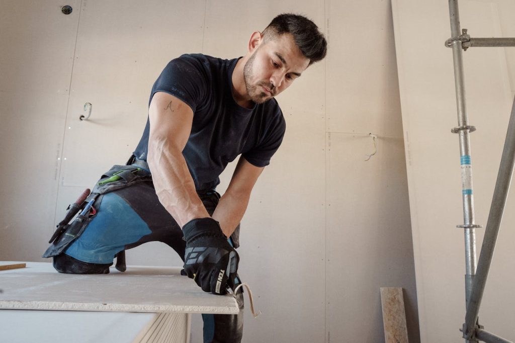 man-cutting-a-plasterboard-11427405 Man in gloves cutting plasterboard for drywall installation inside a building.