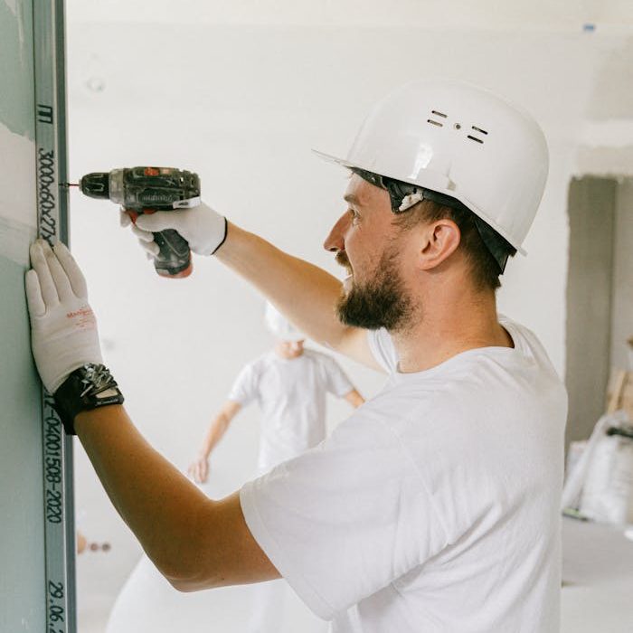Adult male in safety gear using a power drill on a construction site indoors.